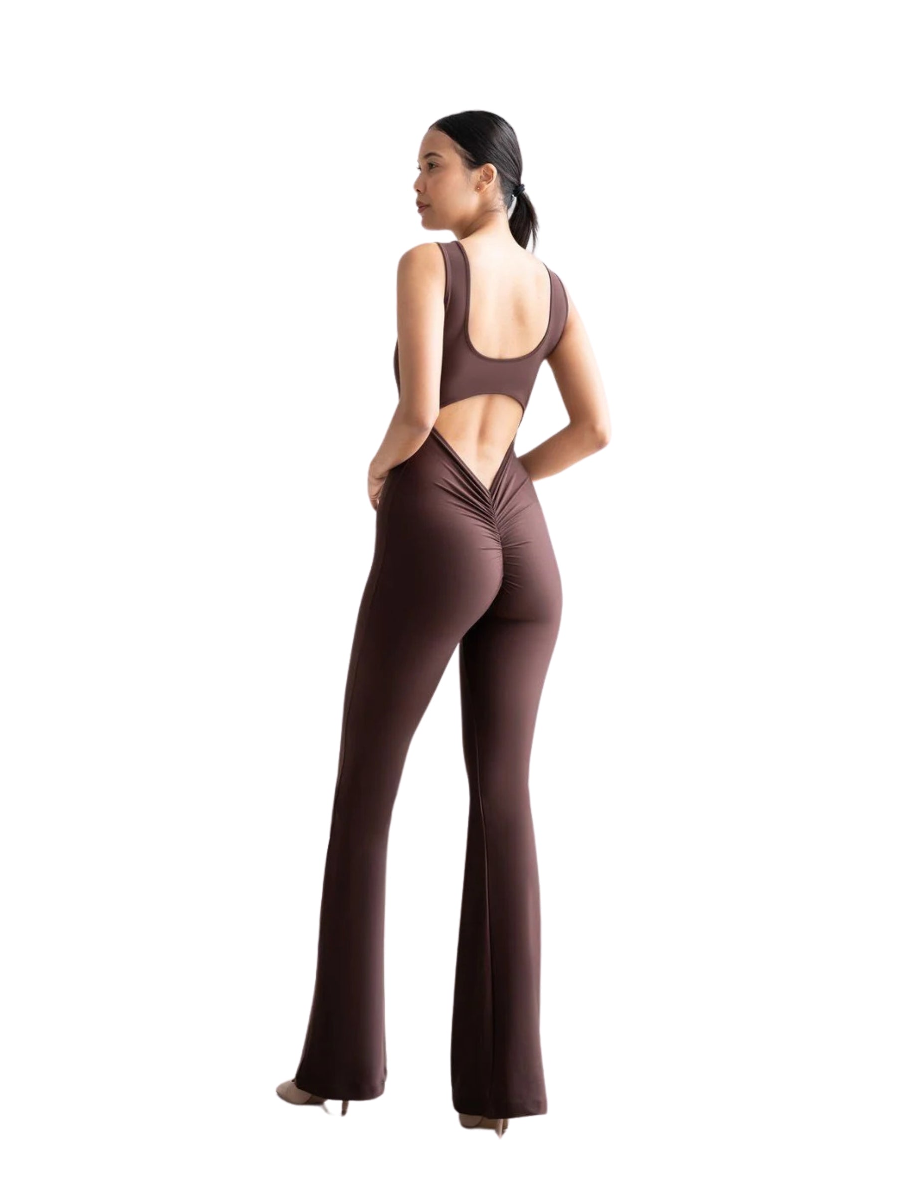 Frau in Lisminas 1505 Spanish Scrunch Butt Jumpsuit, Braun, offener Rücken, Schlaghosen-Stil, seitliche Pose mit Absätzen.